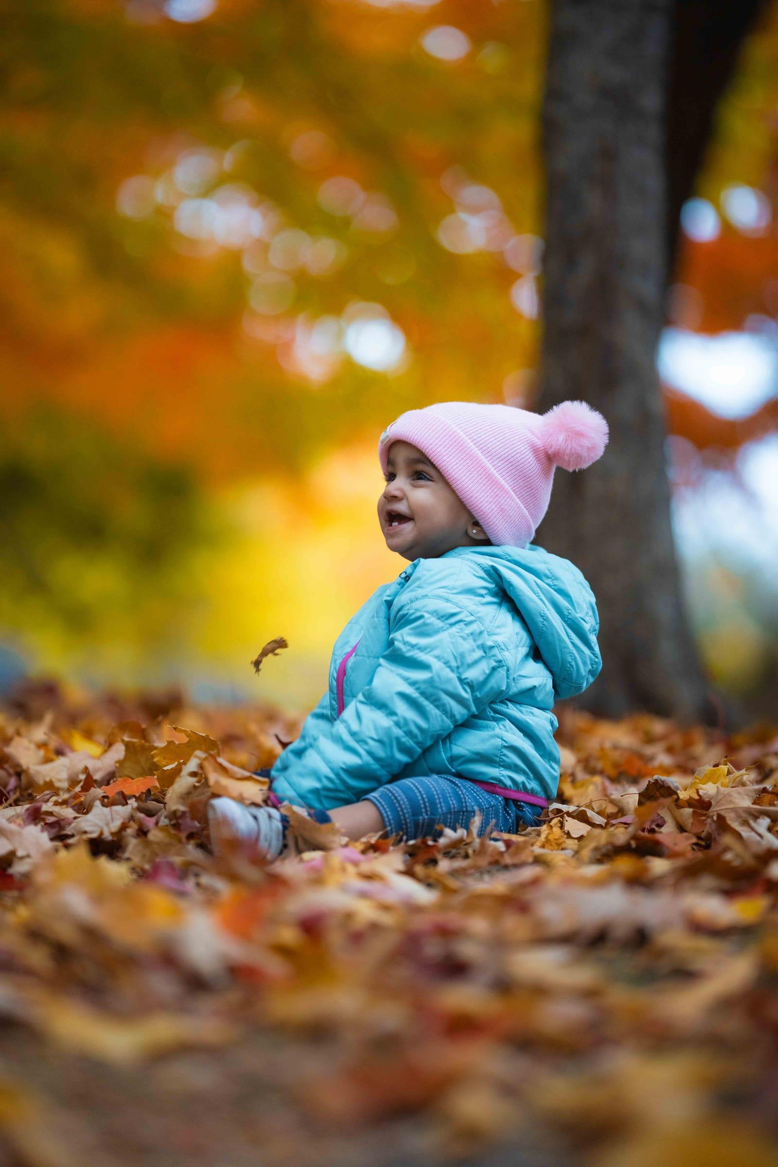 Child in a pom-pom hat surrounded by orange fall leaves