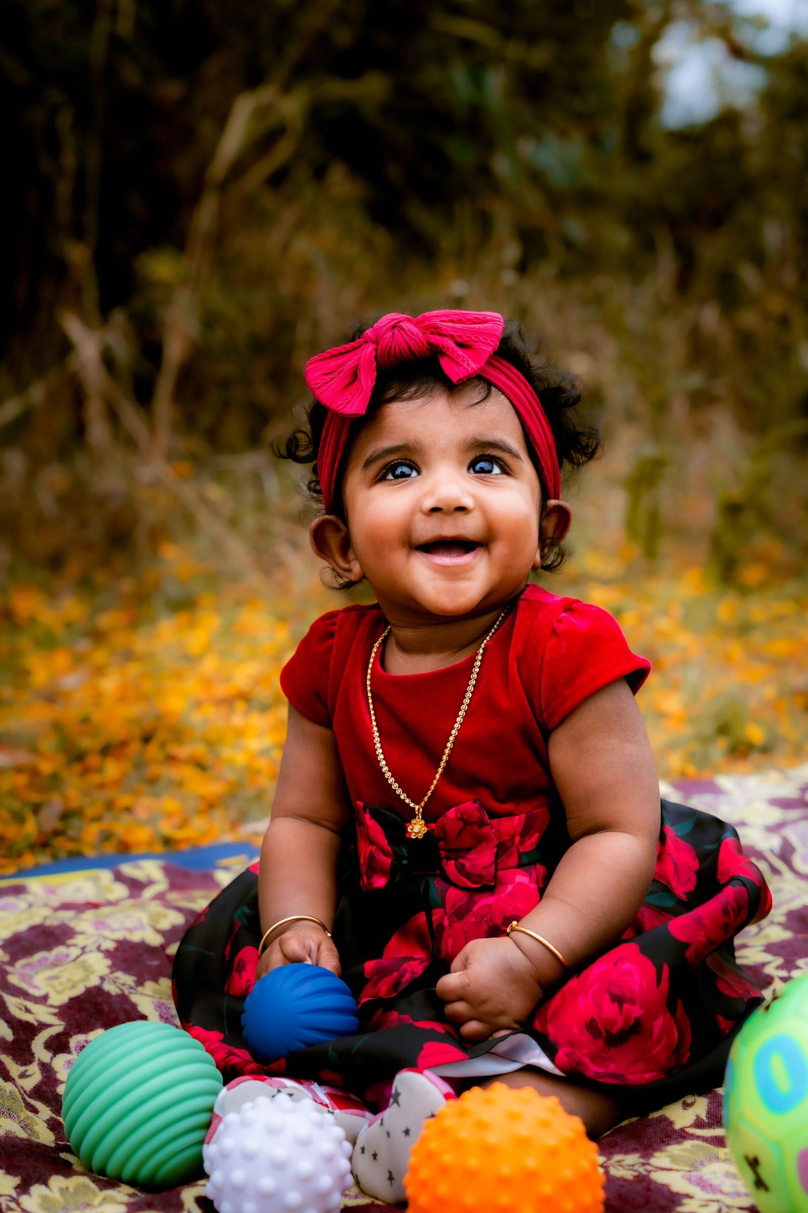 Laughing baby girl in a red dress with colourful balls