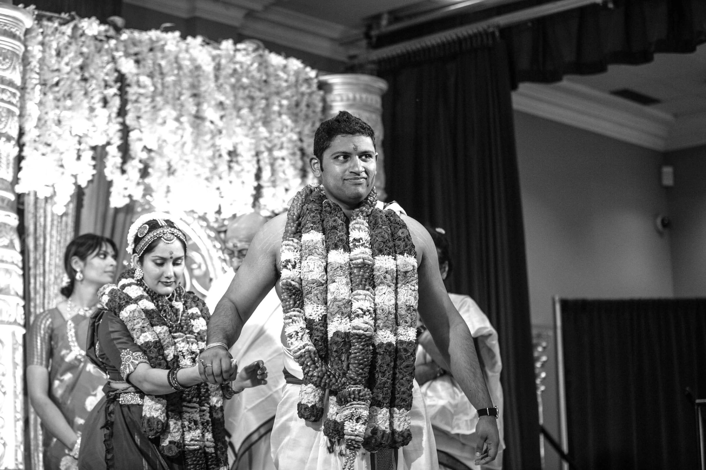 Black and white documentary moment of a wedding couple with garlands
