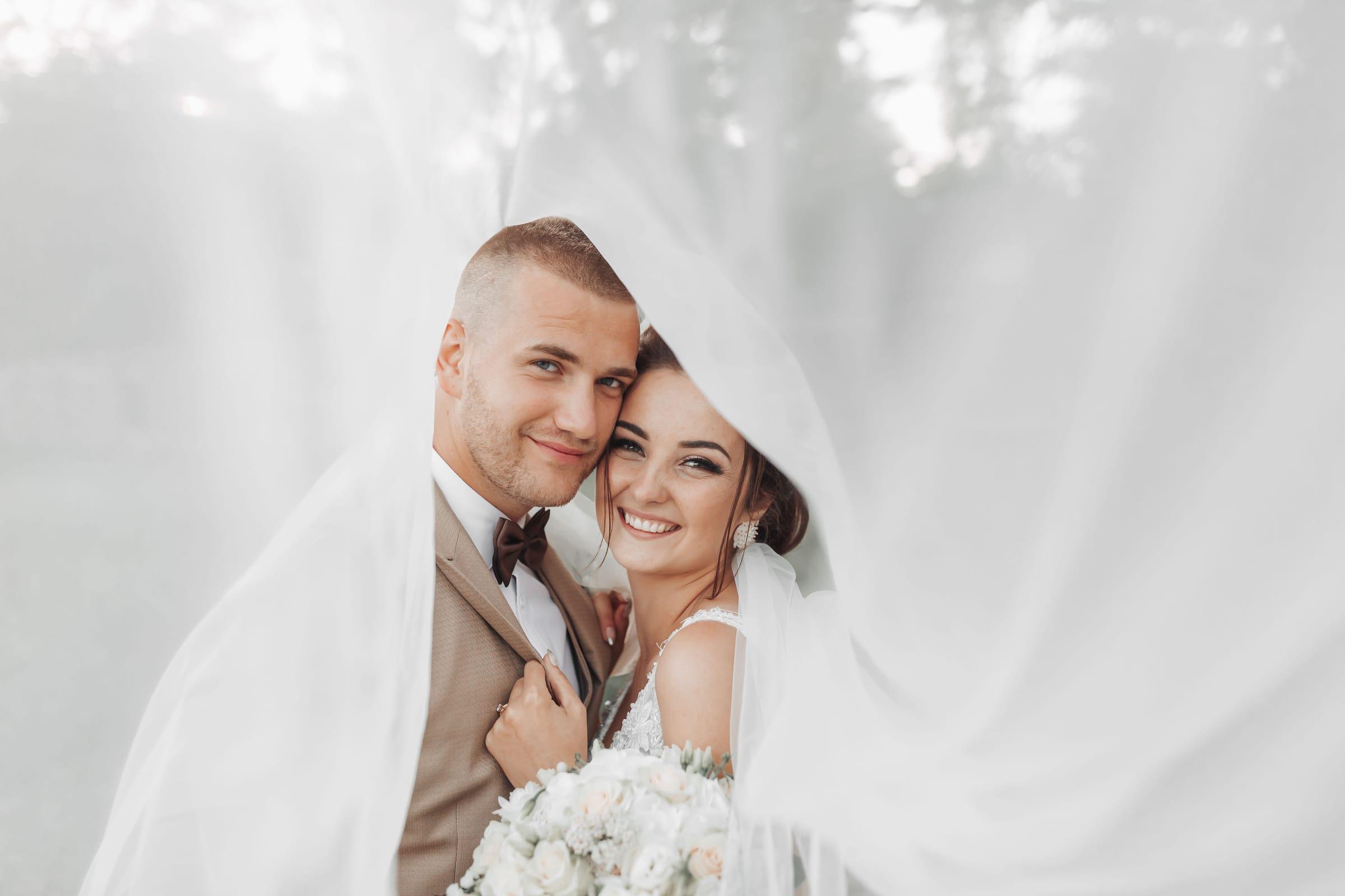 Newlyweds wrapped in the bride's veil, light and airy wedding photography